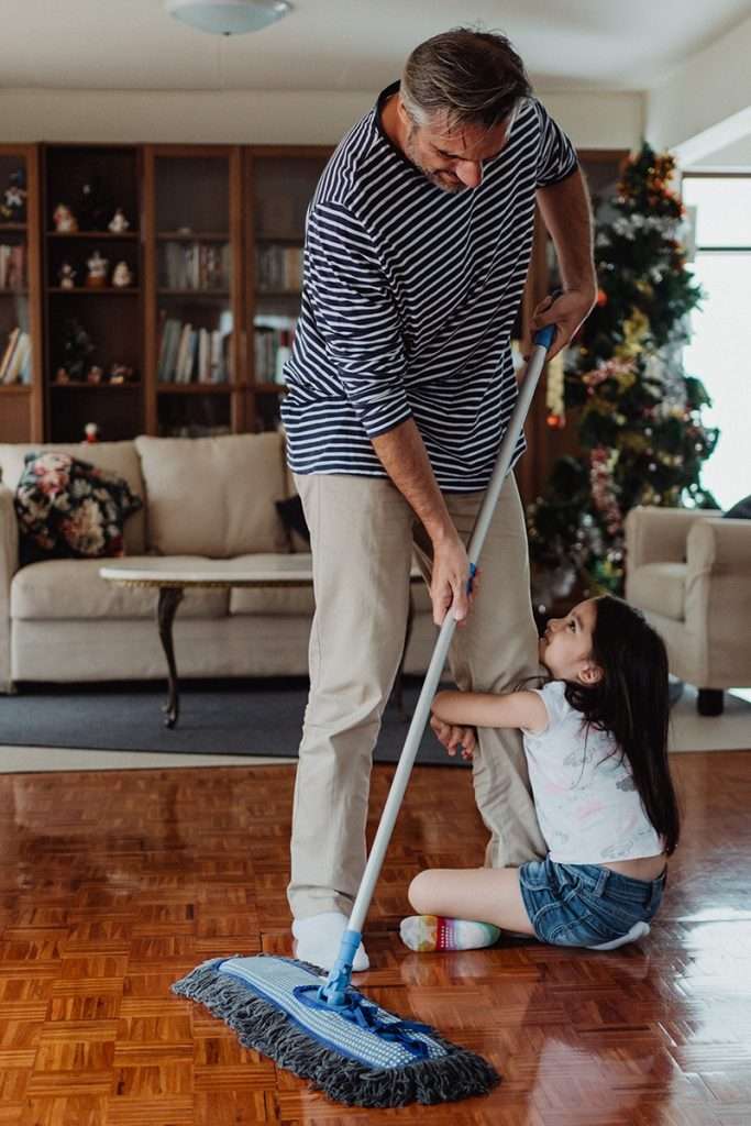 Little girl holding onto a man's leg as he uses a non toxic floor cleaner