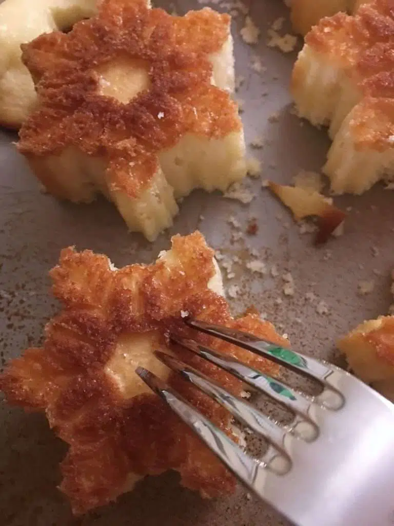 Fork poking holes into freshly baked cream of coconut poke cakes on a baking sheet.