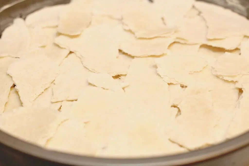 A round pan with pieces of torn tortillas spread through out the pan. 