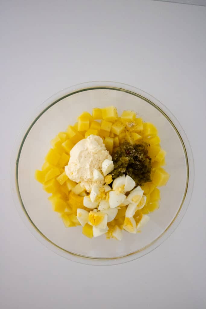 Southern Potato Salad Recipe (My Mom's Famous Recipe) 6 Overhead view of cooked cubed potato, mayonnaise, pickle relish, chopped boiled eggs, and white vinegar in a mixing bowl.