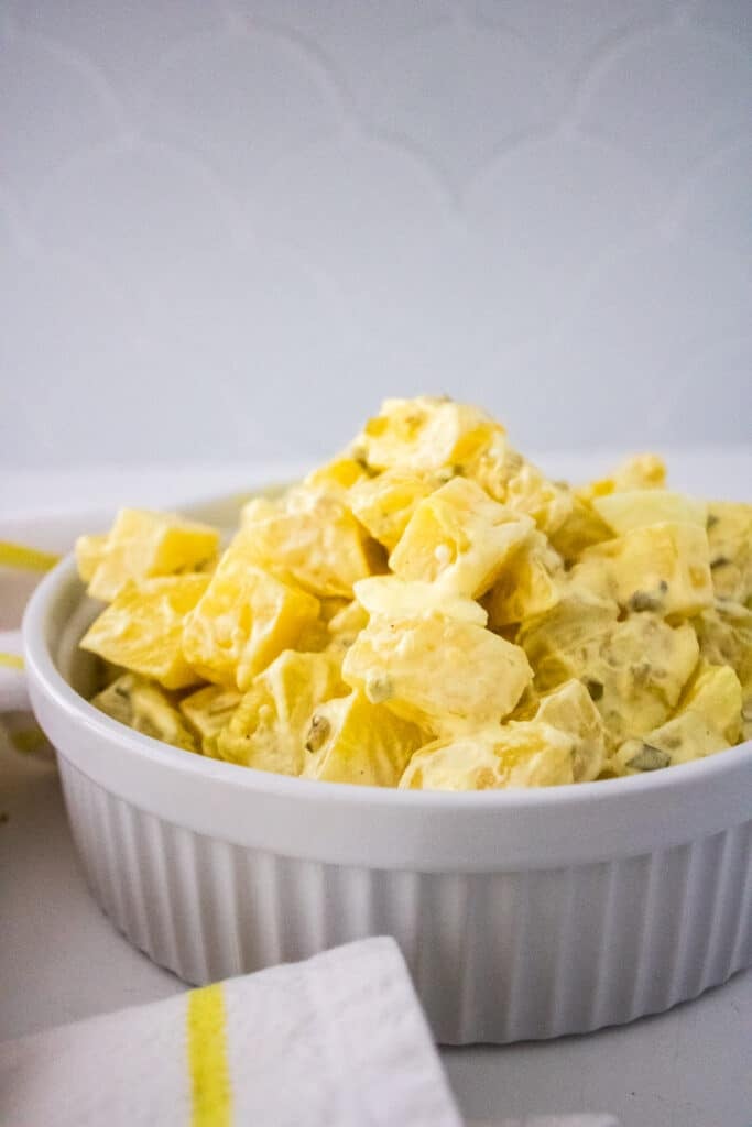 Recipe Index 21 Southern potato salad in a white serving bowl, white and yellow checkered kitchen towel on a white countertop.