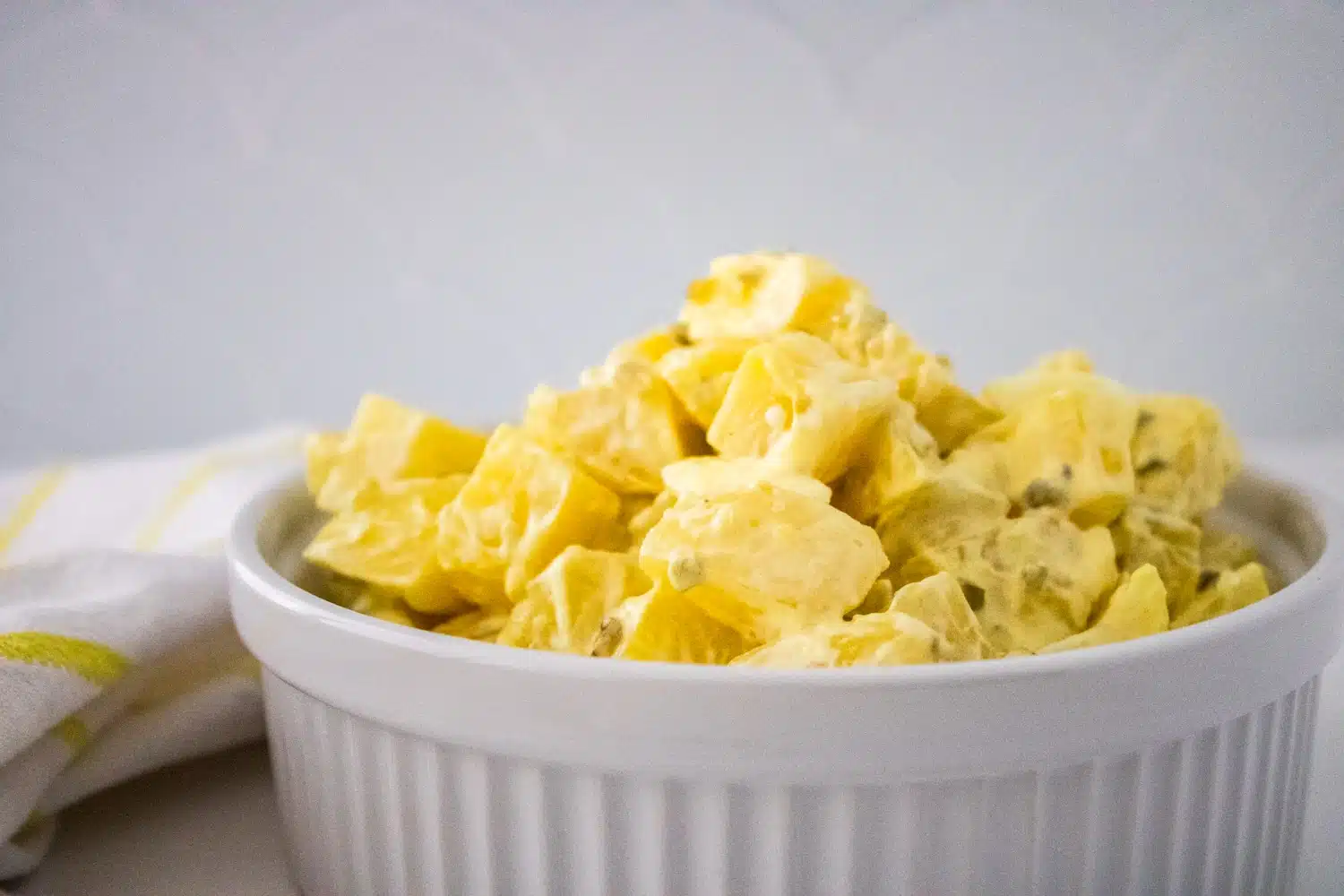 Southern Potato Salad in a white serving bowl, white and yellow checkered kitchen towel.