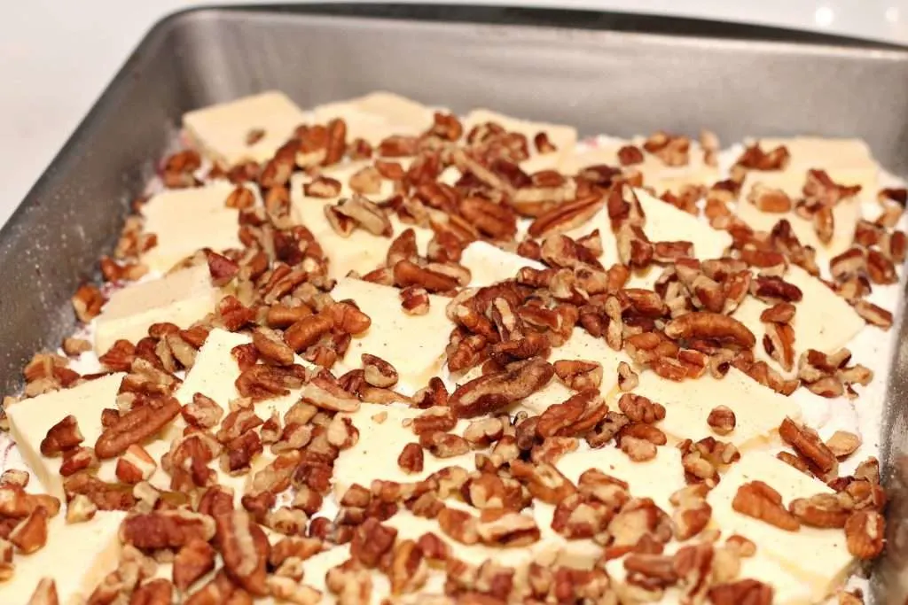 Cherry Pineapple Dump Cake (Only 5 Ingredients and 1 Pan!) 9 Cherry pineapple filling in pan topped with dry cake mix and pats of butter on top along with pecans spread out over top of pan