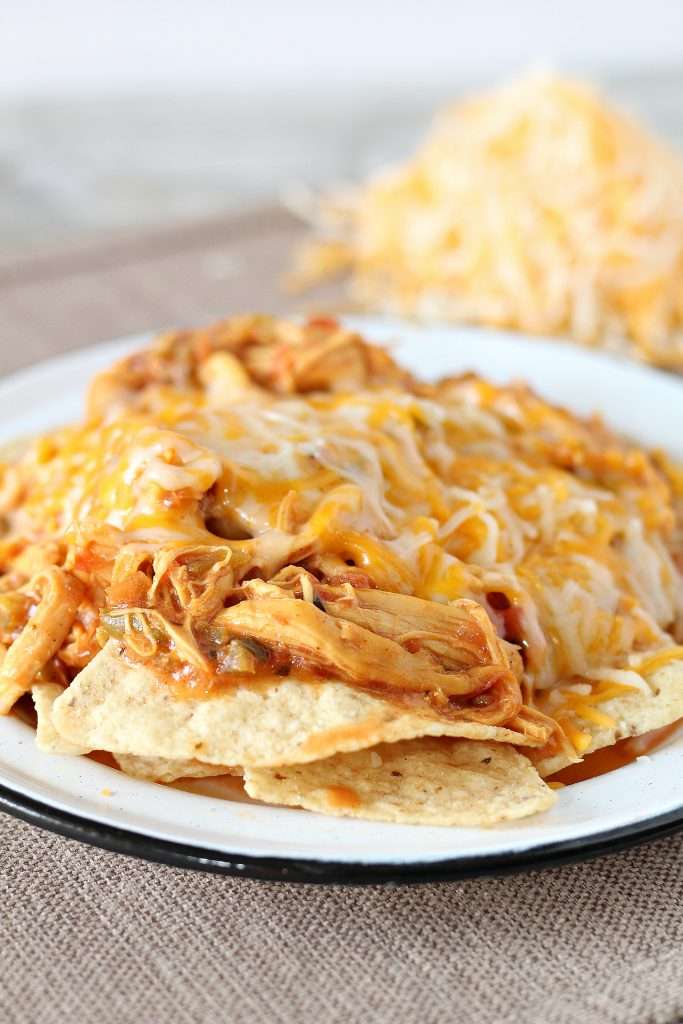 Crockpot Chicken Nachos on a white plate, topped with melted shredded cheese. 