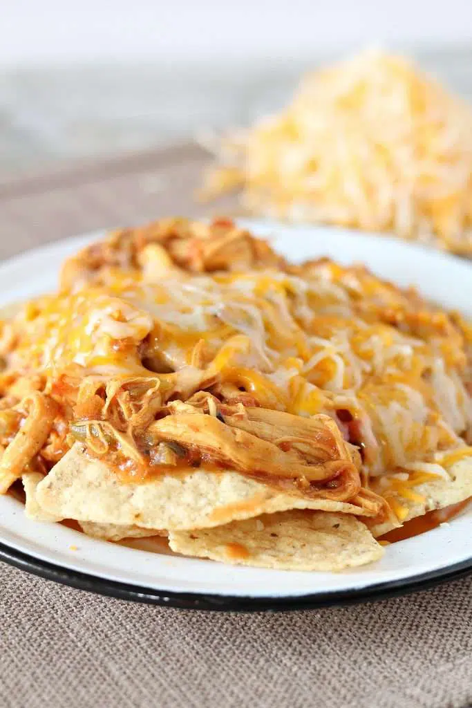 Crockpot Chicken Nachos on a white plate, topped with melted shredded cheese. 