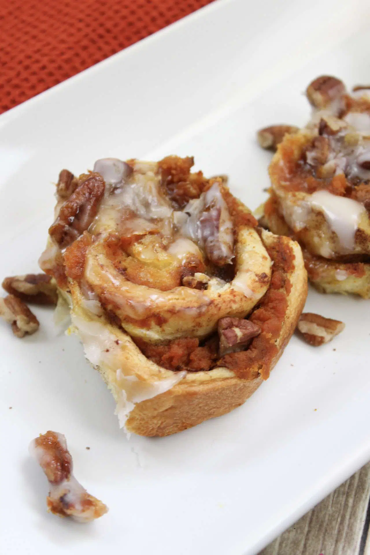 Closeup high angle shot of the finished Pumpkin Cinnamon Rolls topped with sugar glaze, on a white platter.
