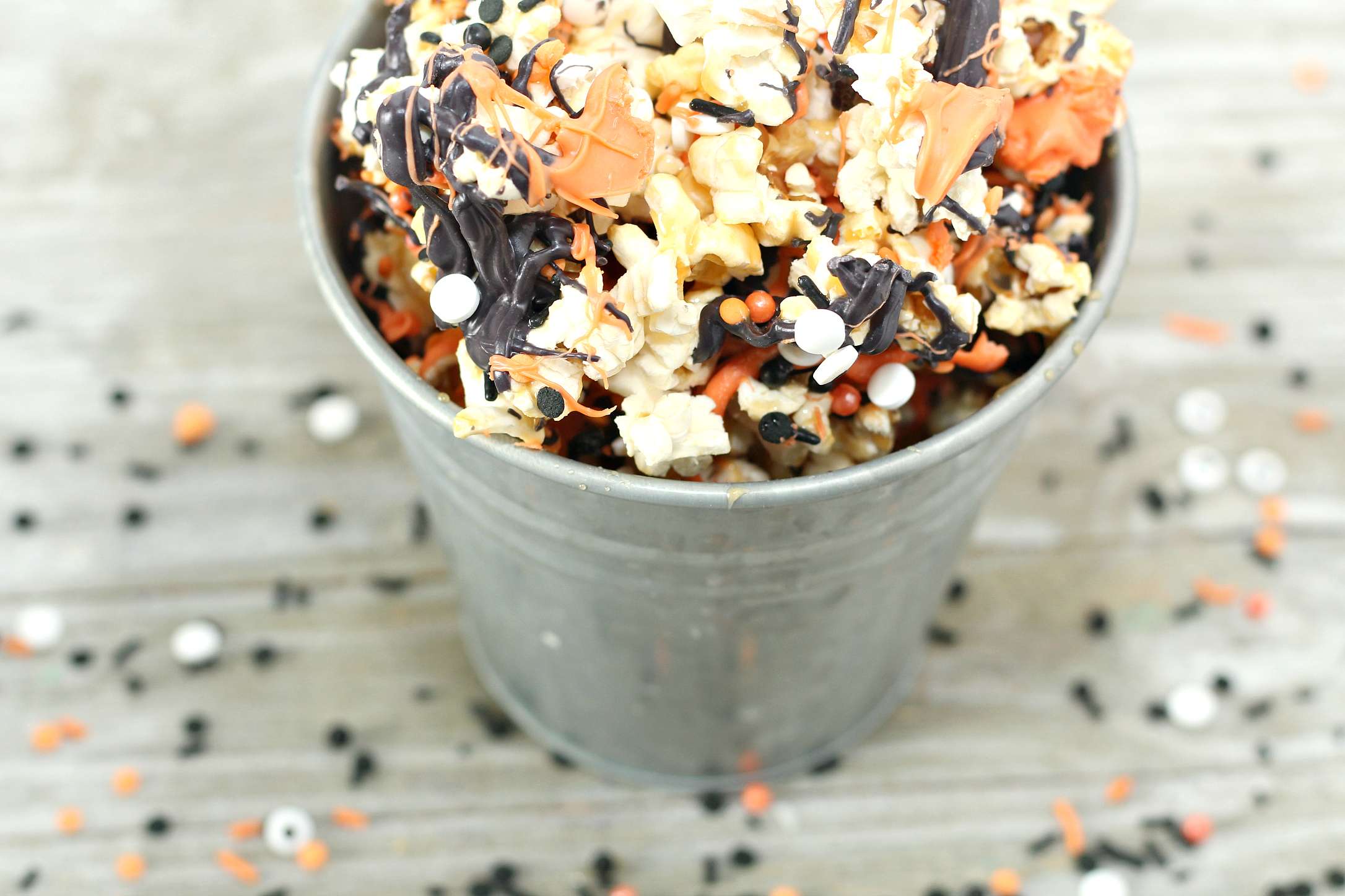 Overhead view of Halloween popcorn in a metal bucket on a wooden countertop.