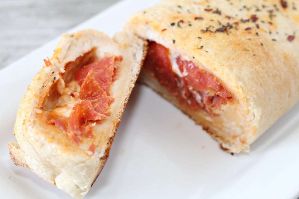 The finished Spicy Stuffed Pizza Bread on a platter, with its tip sliced off to reveal the interior.
