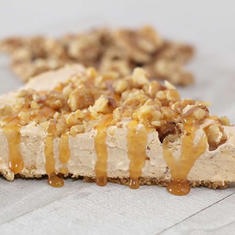 Slice of no bake pumpkin cheesecake topped with chopped walnuts and caramel topping.