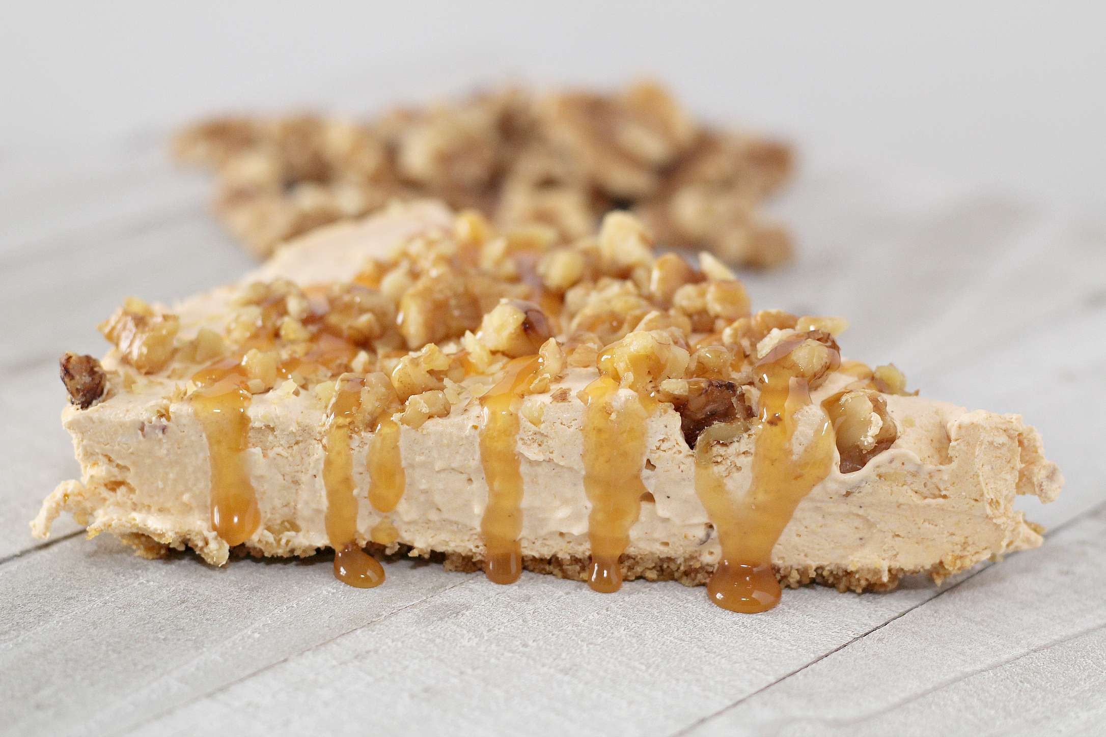 Slice of no bake pumpkin cheesecake topped with chopped walnuts and caramel topping.