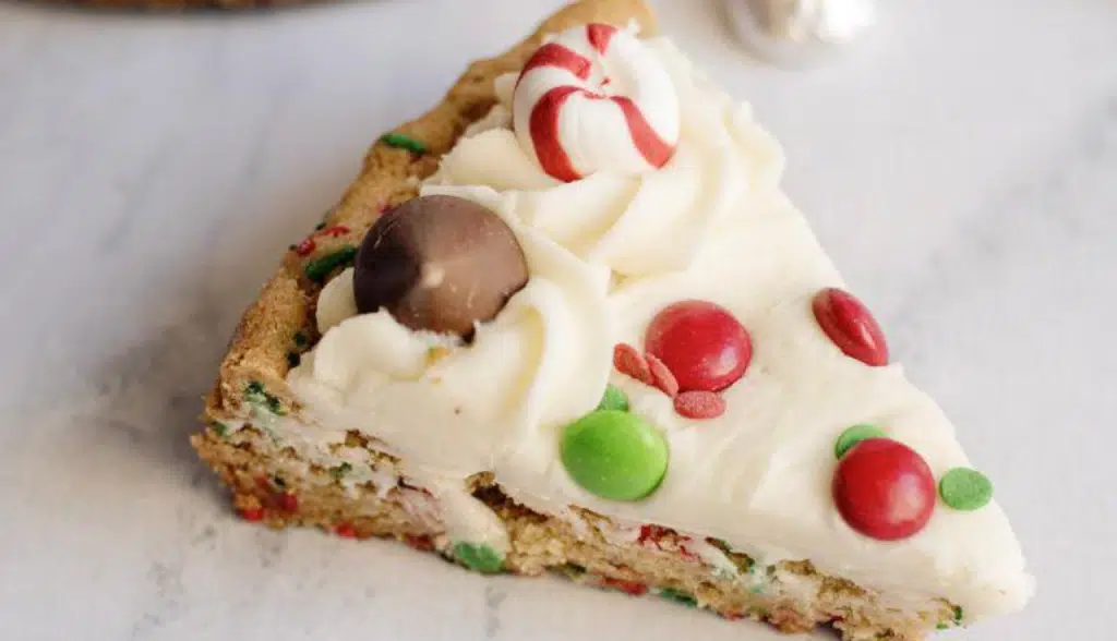 A slice of Christmas cookie cake with frosting and Christmas colored candy.