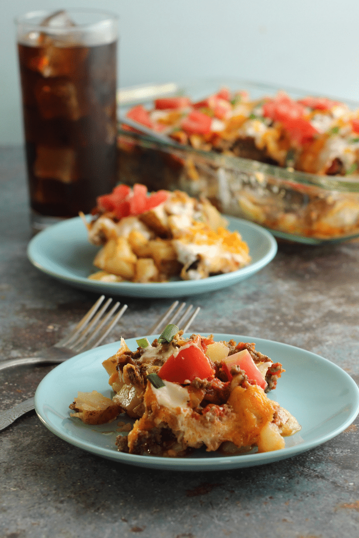 Easy Taco Bake 2 taco potato bake on blue plates with forks and drink in back