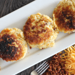 Mashed potato fritters on a white plate, metal fork on a wooden countertop.