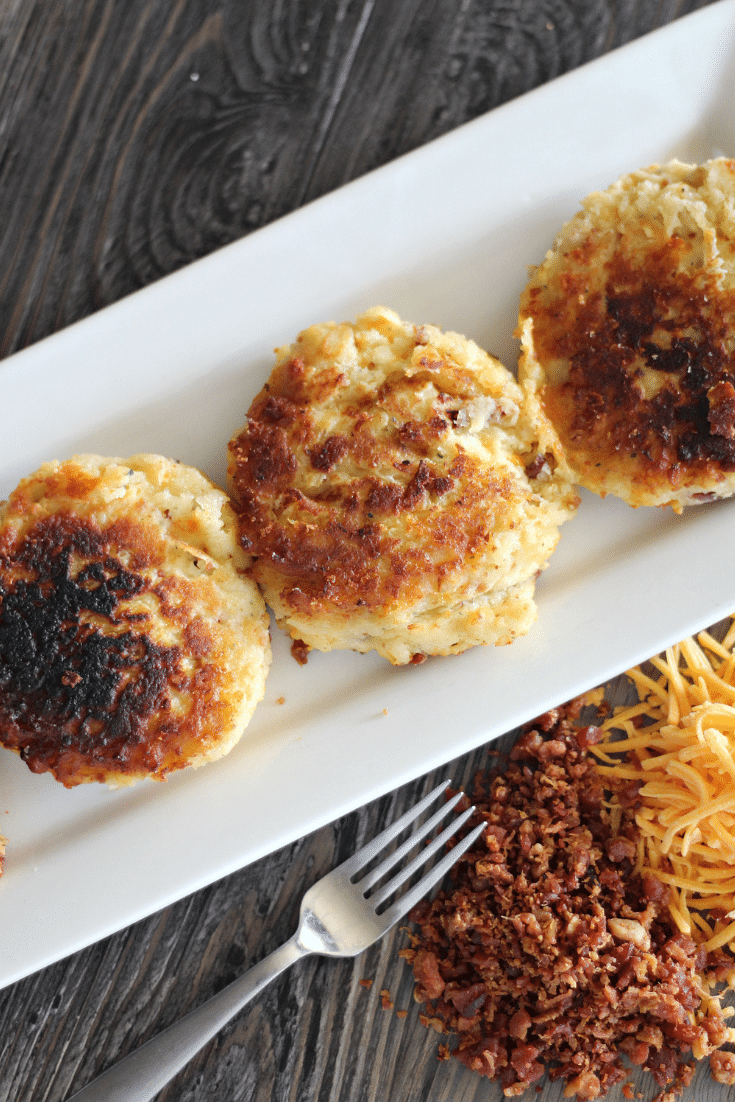 Mashed potato fritters on a white plate, metal fork on a wooden countertop.