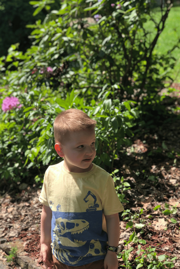 child outside standing by bushes