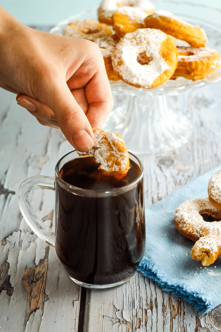 A hand dunking an Old Fashioned donut in a cup of black coffee.