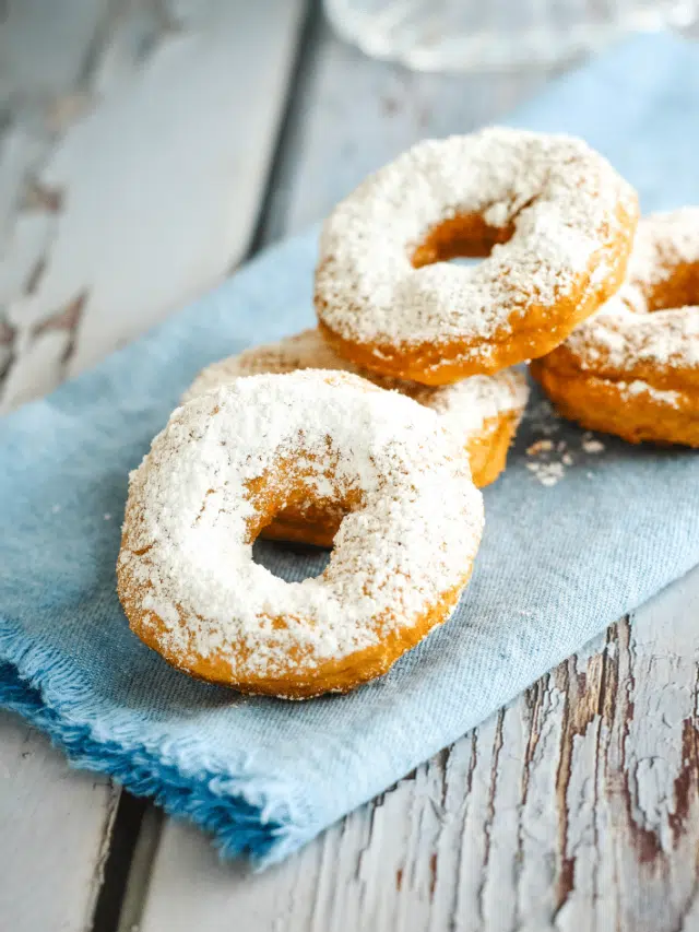 4 old fashioned donuts on blue napkin that's placed on a wooden surface.