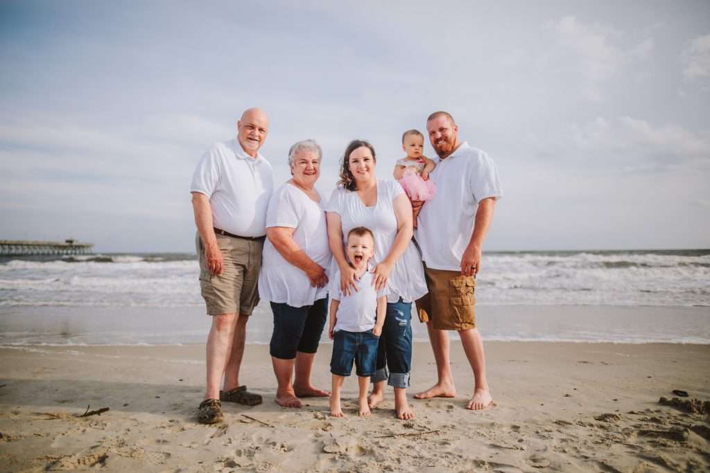 Three generation family photo on the beach in matching white shirts, jeans and khaki pants 