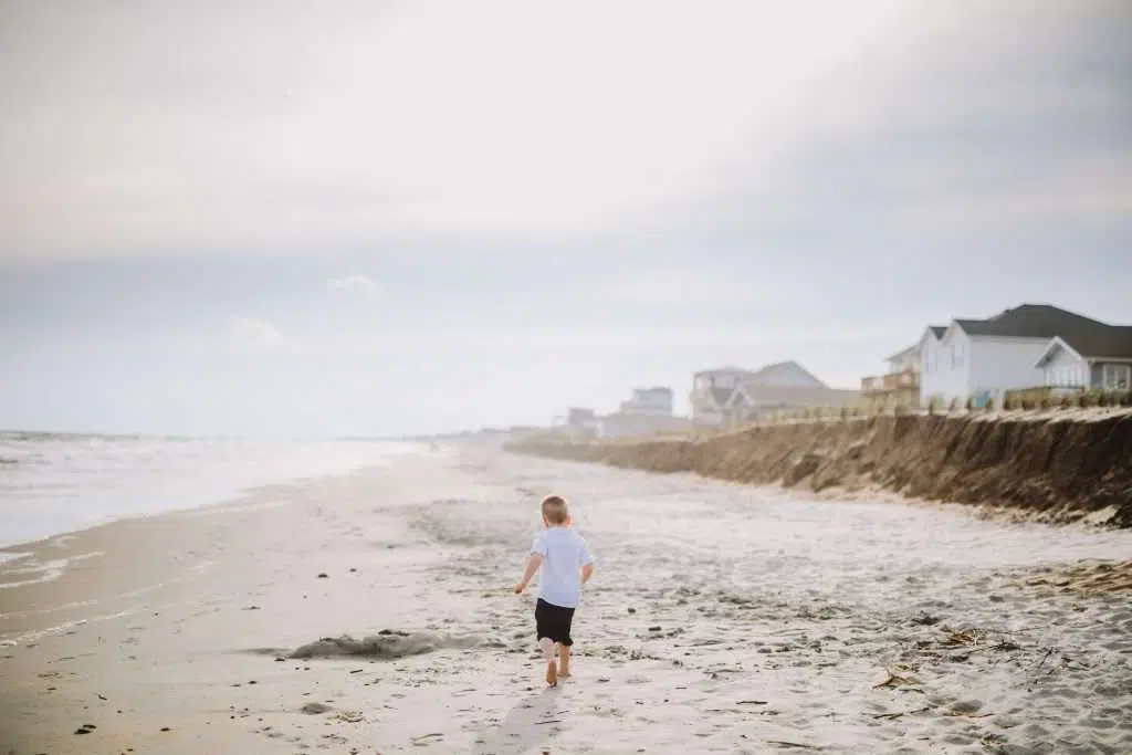 Toddler boy running down beach in white shirt and jean shorts