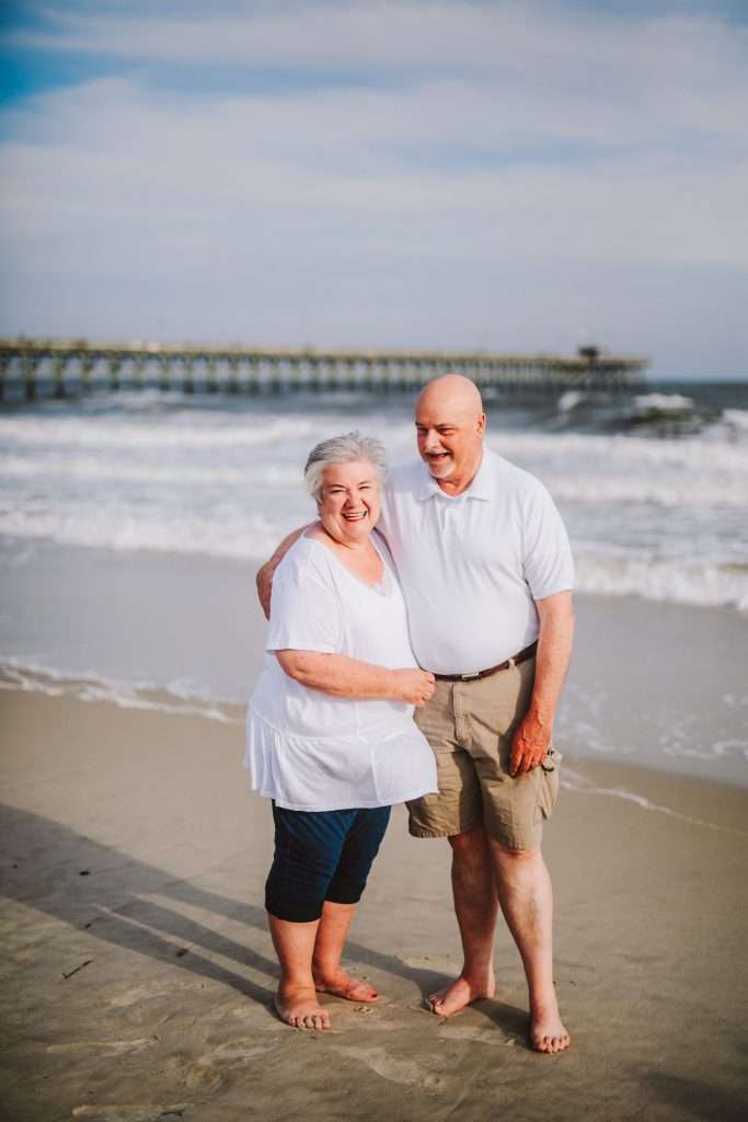 Grandparents laughing at photo session on beach in matching white shirts