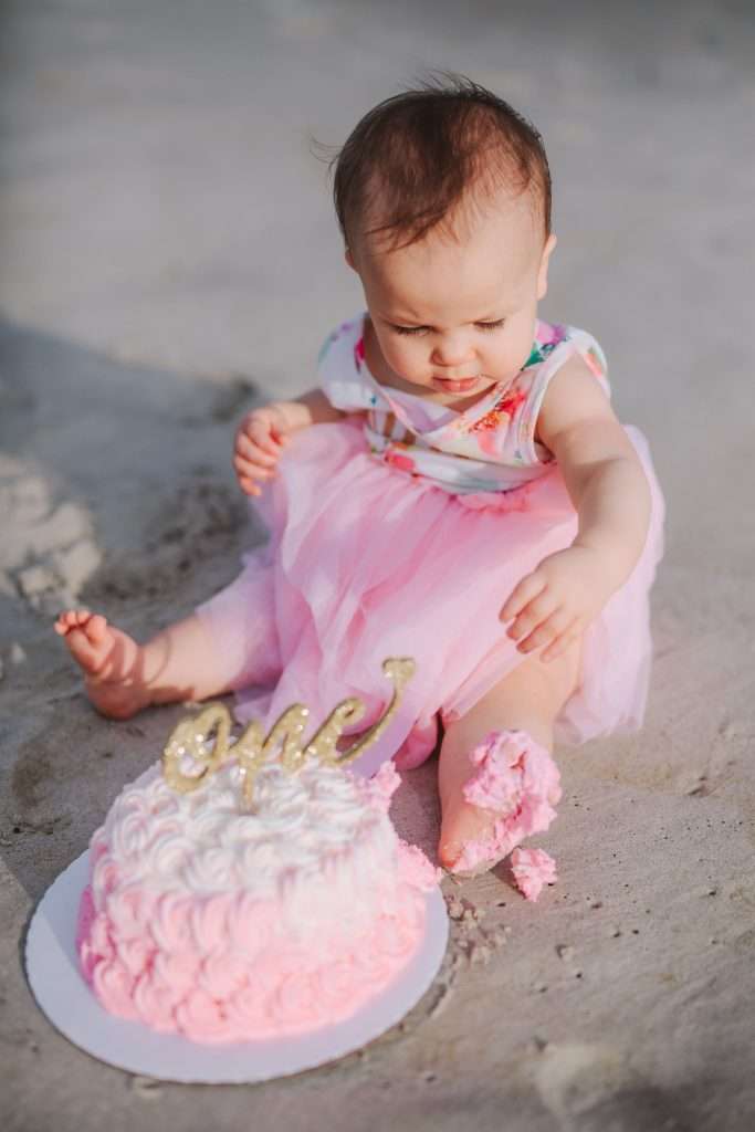 One year old with pink rosette cake and gold cake topper on beach