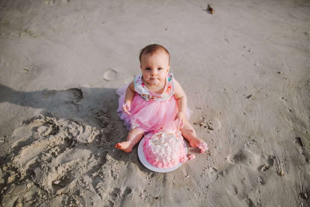 One year old in pink tutu with pink rosette cake on beach 