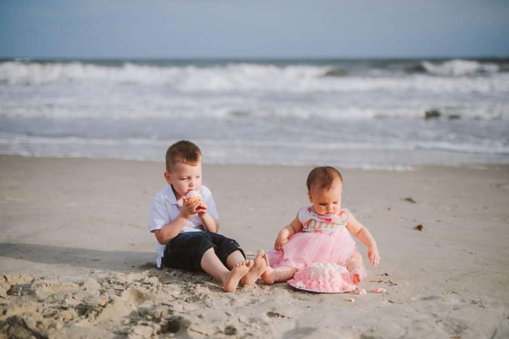 Toddler big brother and one year old on beach for cake smash session