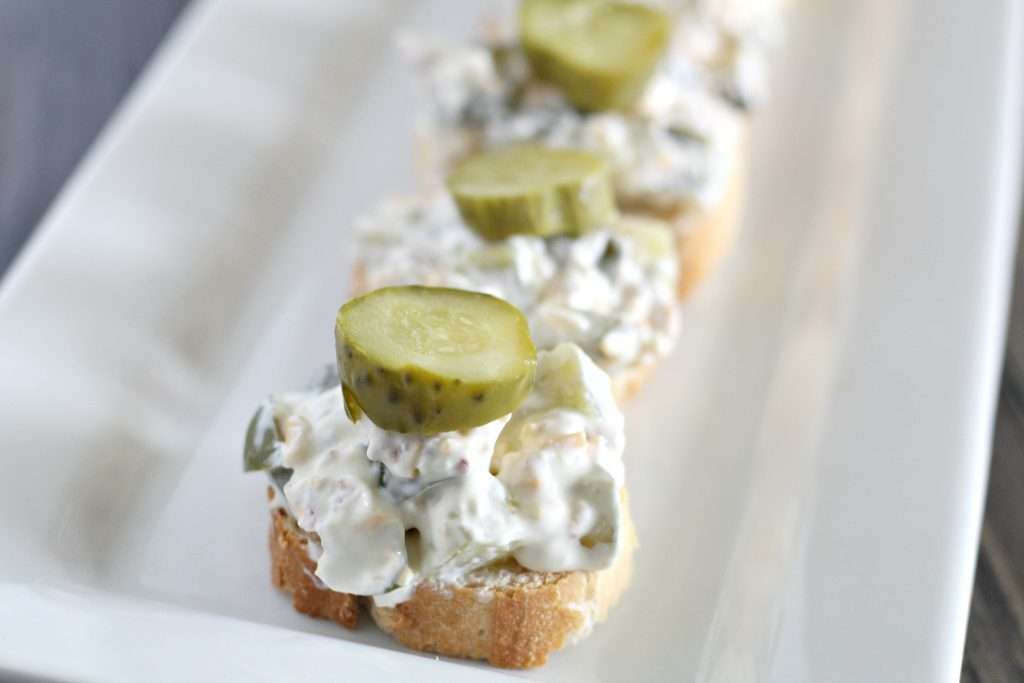 Delicious and Easy Dill Pickle Dip 6 dill pickle dip on french bread on white platter topped with dill pickles