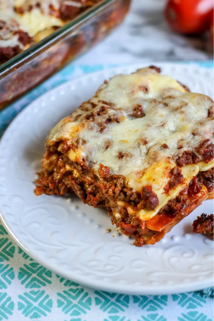 A single serving of ravioli casserole on white plate, remainder of casserole in the background.