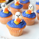 Ghost shaped candy on top of blue frosted cupcakes on a serving white plate.