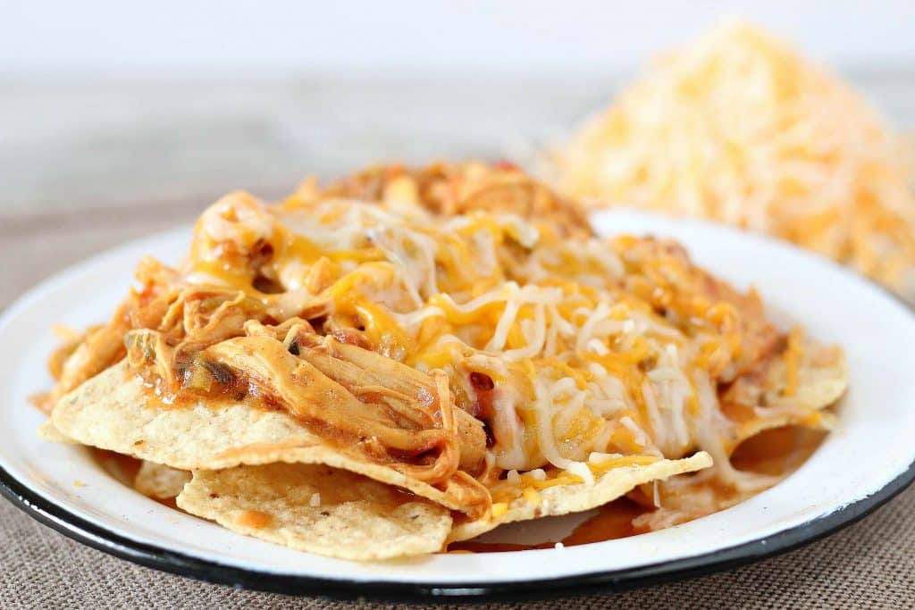 Crockpot chicken nachos with shredded cheese on a white plate. 