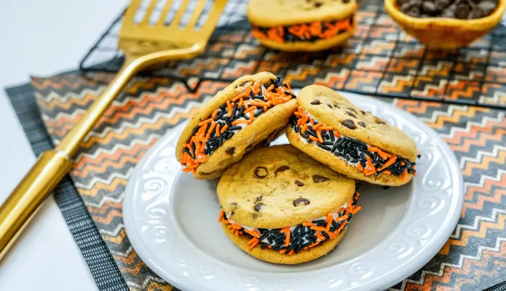 Chocolate Chip Halloween Cookies 14 Three chocolate chip Halloween cookies on a white plate, additional decorative Halloween cookies on a cooling rack on a decorative mat.
