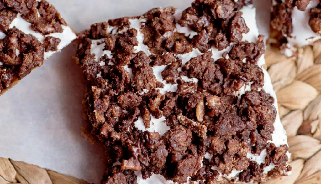 Close up, flat lay shot of chocolate marshmallow bars on a sheet of parchment paper that has been placed on a rattan mat.