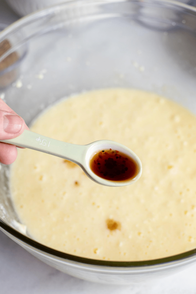 Chocolate Marshmallow Bars 13 A hand holding a measuring spoon with vanilla extract that's hovering above a glass bowl with whipped butter mixture.