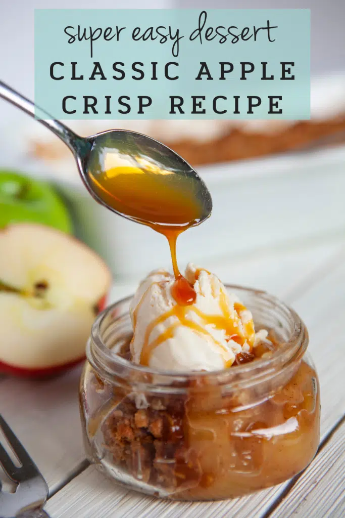 Jar of easy apple crisp topped with ice cream or a dollop of whipped cream with metal spoon drizzling caramel sauce over, freshly sliced apples, baking dish with easy apple crisp in the background.