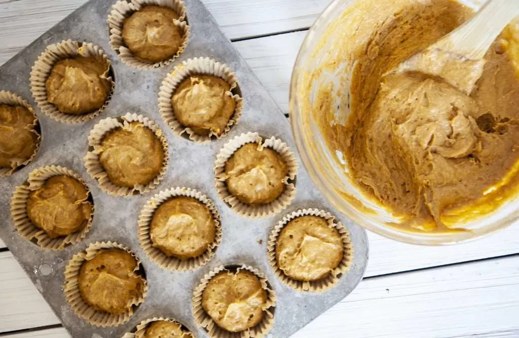 glass bowl of pumpkin muffin mixture and mixture filling a dozen muffin tins. 