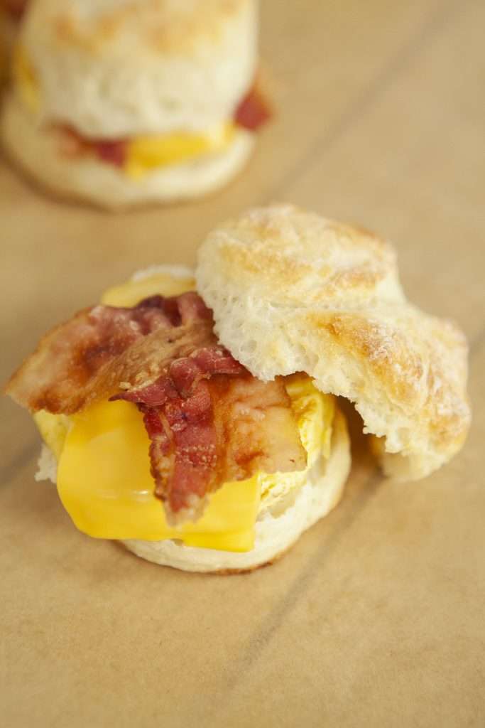 Bacon Egg and Cheese Biscuit (Weight Watchers Recipe) 4 Bacon egg and cheese biscuits with top of biscuit off, on a wooden surface.