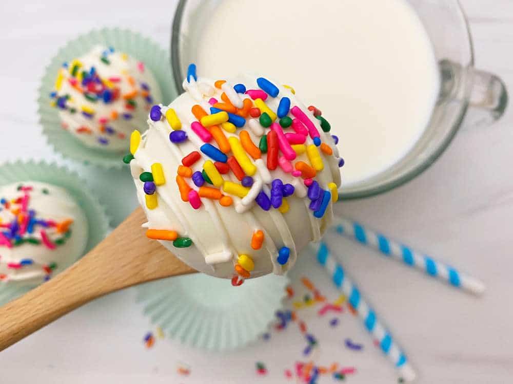 White Chocolate Hot Chocolate Bombs 1 White hot Chocolate Bomb on a spoon with rainbow sprinkles