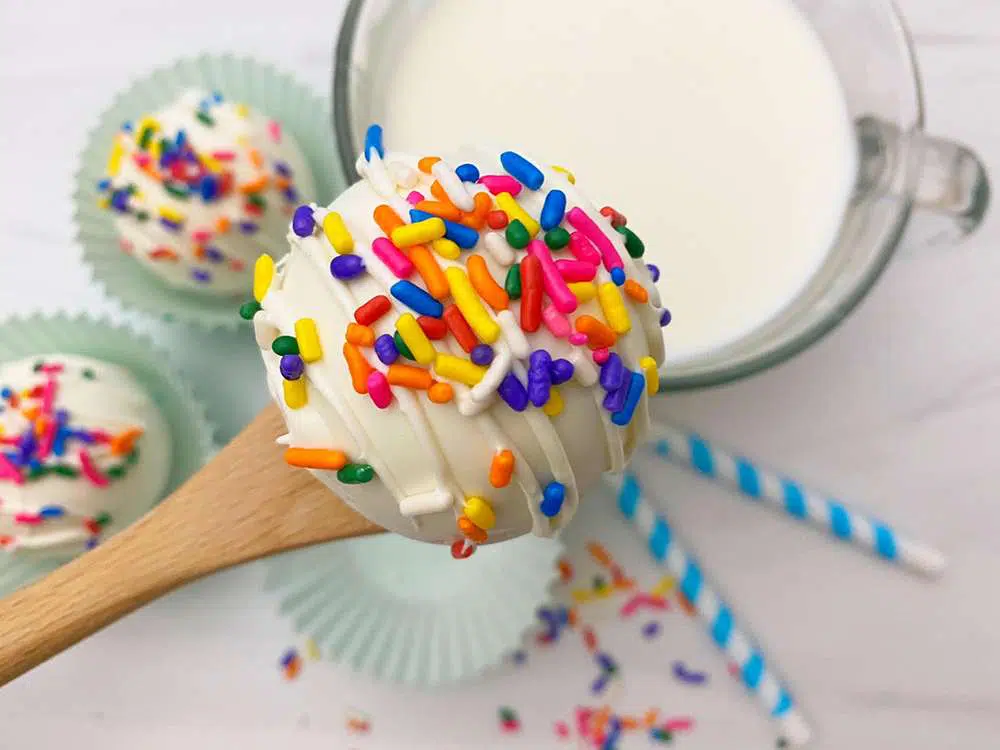 White Chocolate Hot Chocolate Bombs 1 White hot Chocolate Bomb on a spoon with rainbow sprinkles