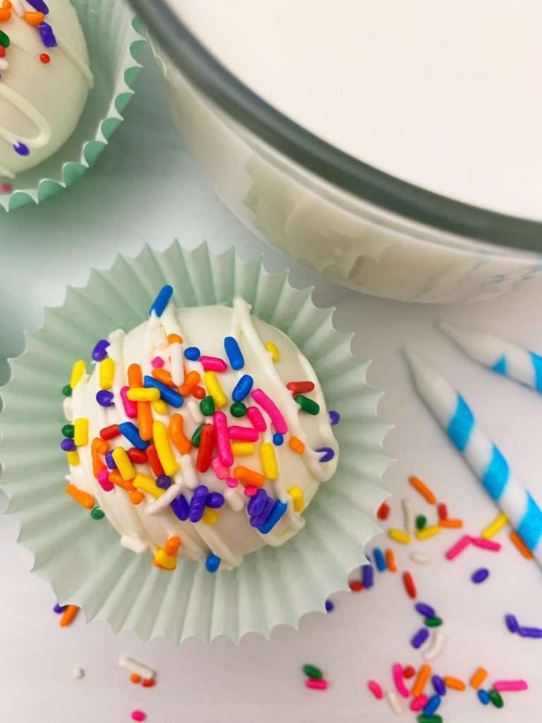 White Chocolate Hot Chocolate Bombs 4 White hot Chocolate Bomb on a spoon with rainbow sprinkles in blue wrapper