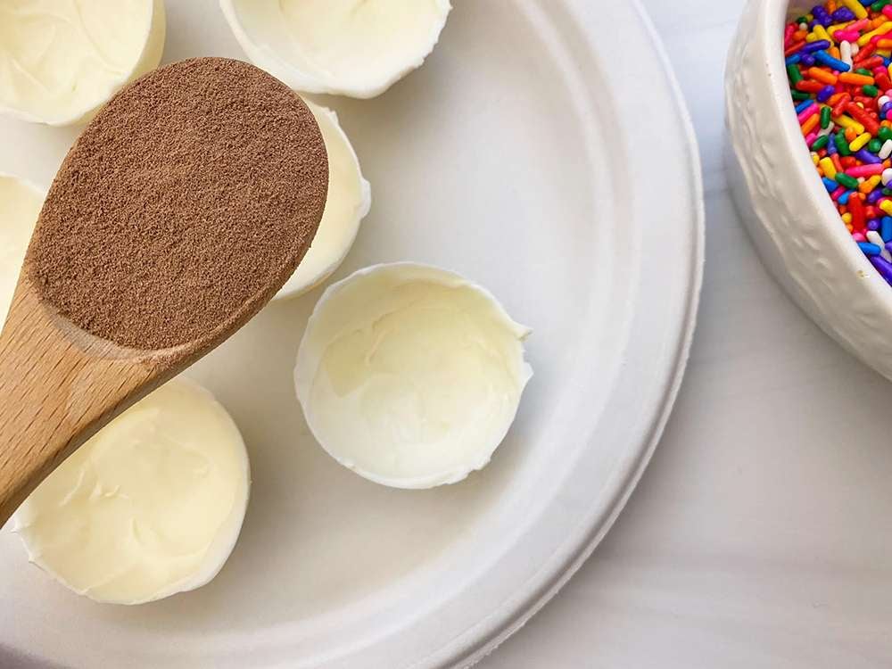Hot chocolate powder on a wooden spoon above white chocolate spheres