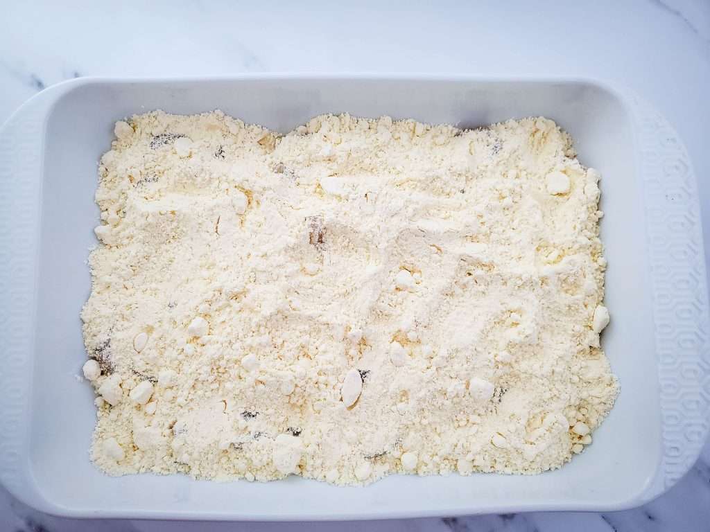 Apple Dump Cake 11 Cake mix sprinkled over apple pie filling in a white baking dish.
