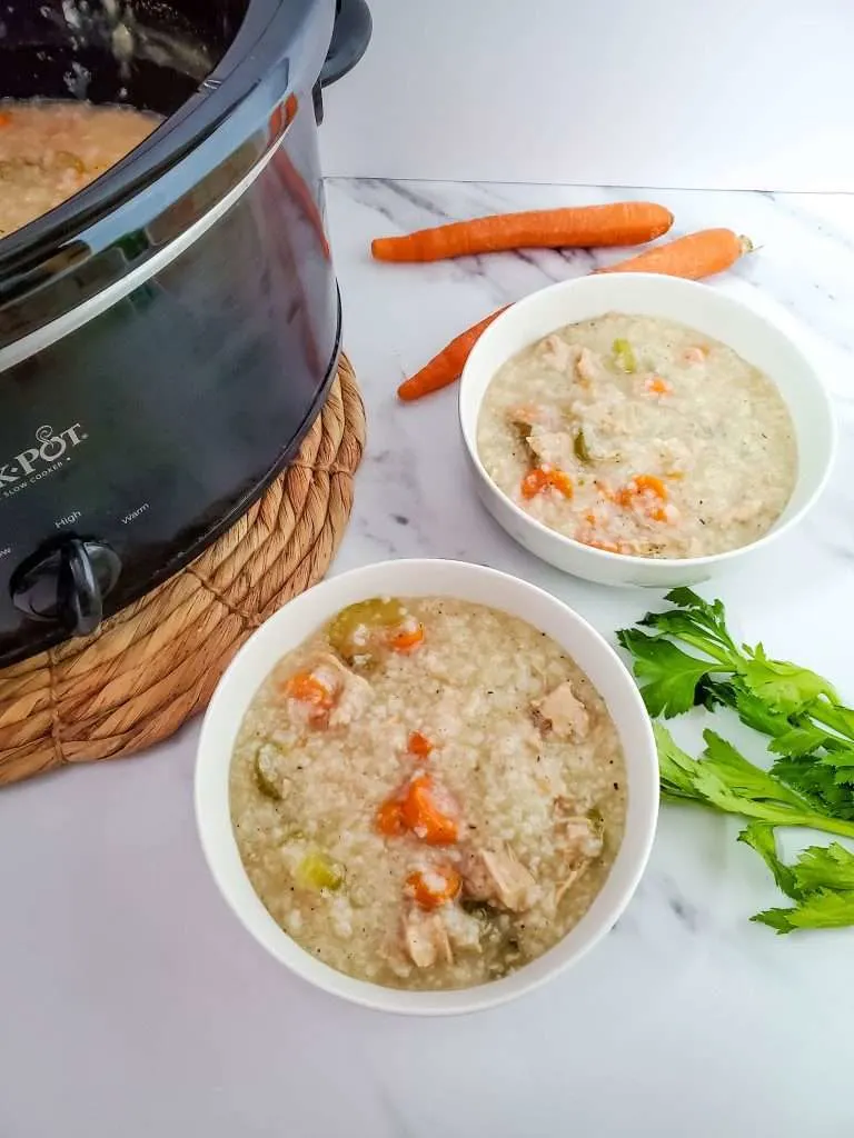 two white bowls of leftover turkey soup with crockpot and carrots in the back