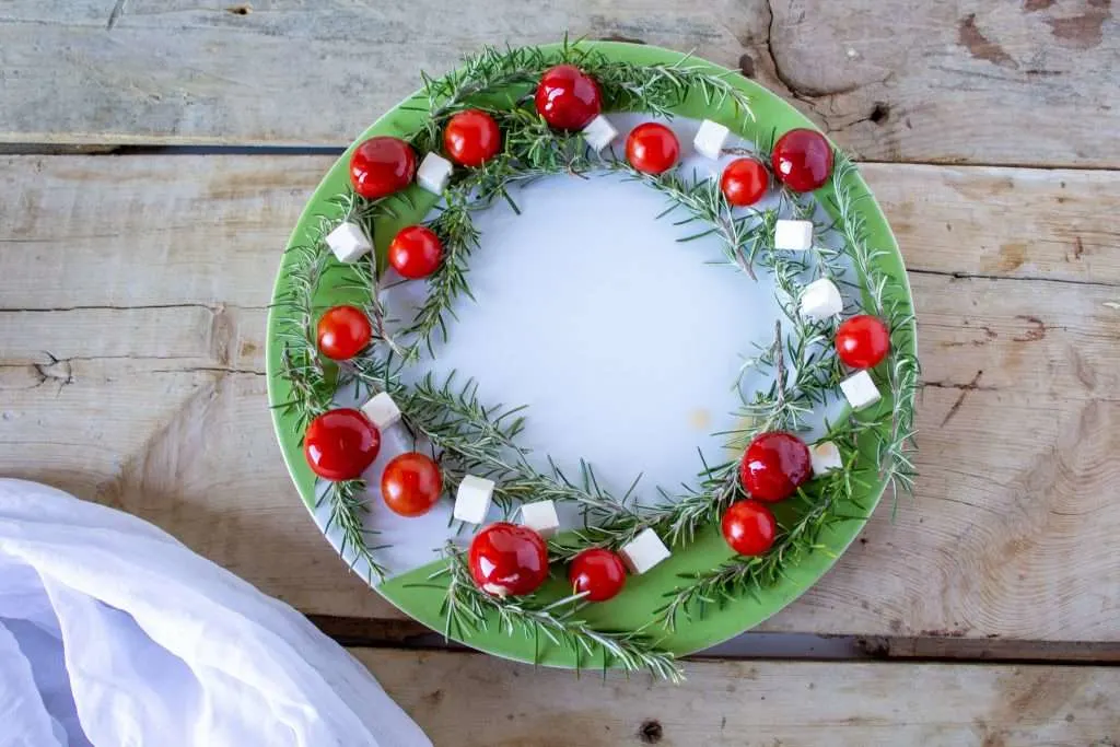 overhead view of tomatoes, feta and rosemary sprigs in circle on white and green serving board