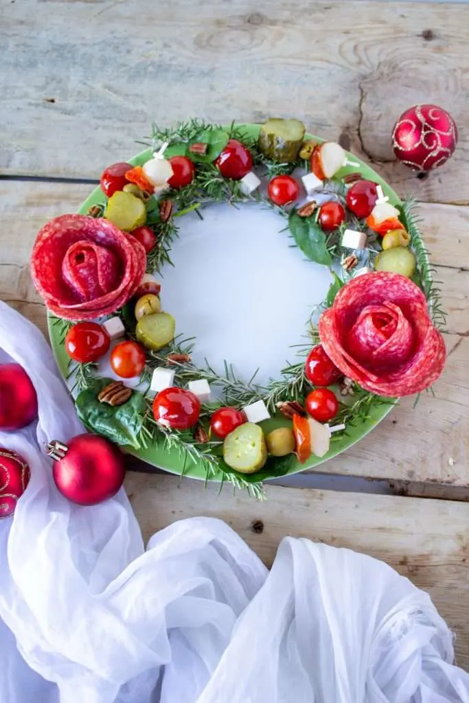 overhead view of Charcuterie Christmas Wreath with rose salami on wooden table with christmas ornaments on side