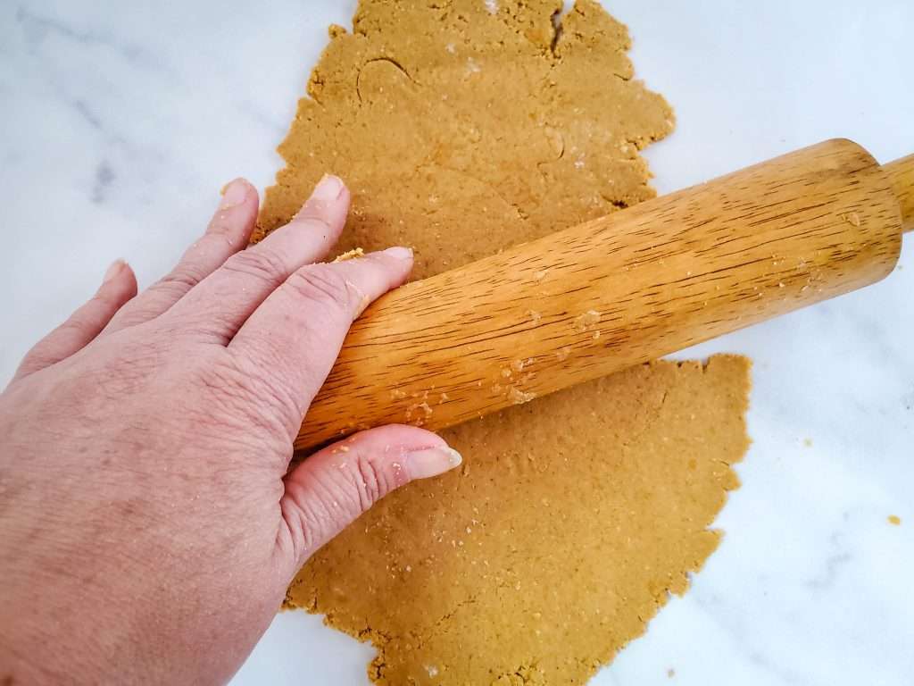 3 ingredient dog treats dough rolled out flat with a rolling pin on a marble surface.