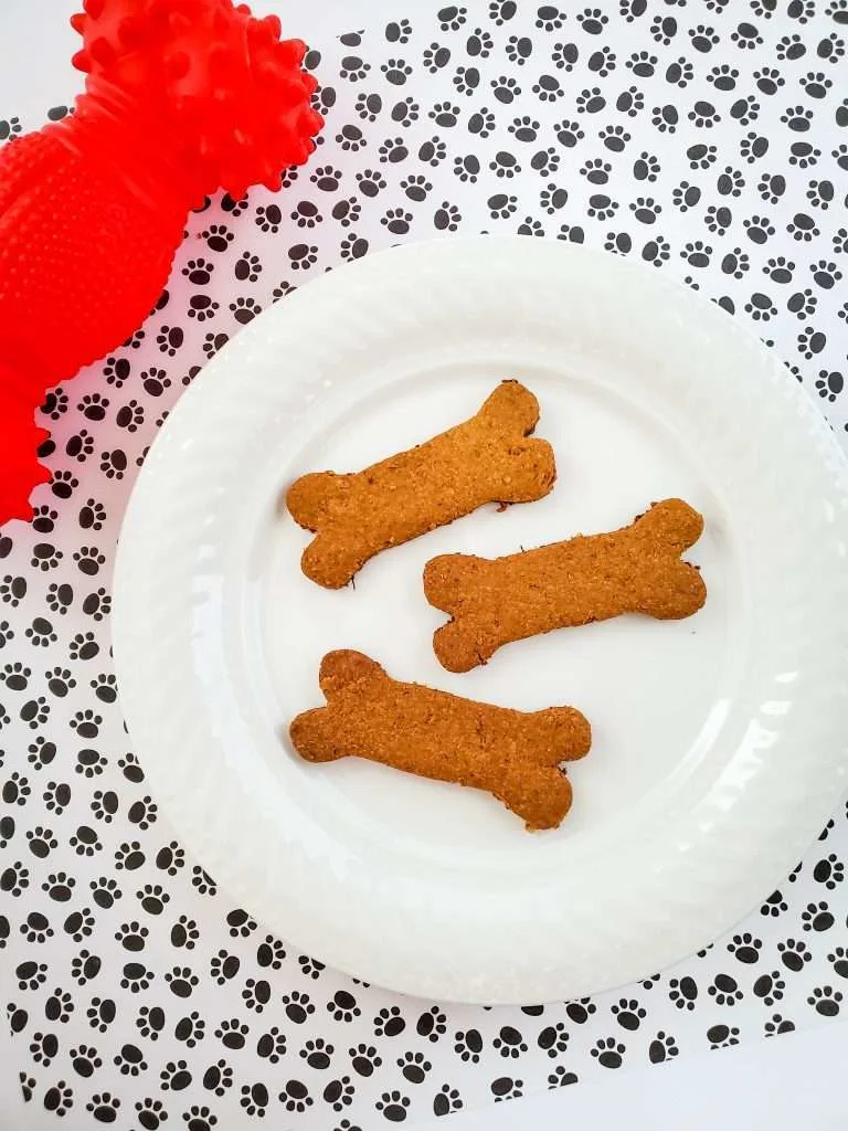 3 Ingredient dog treats on a white plate, dog paw print table cloth with a dog toy.