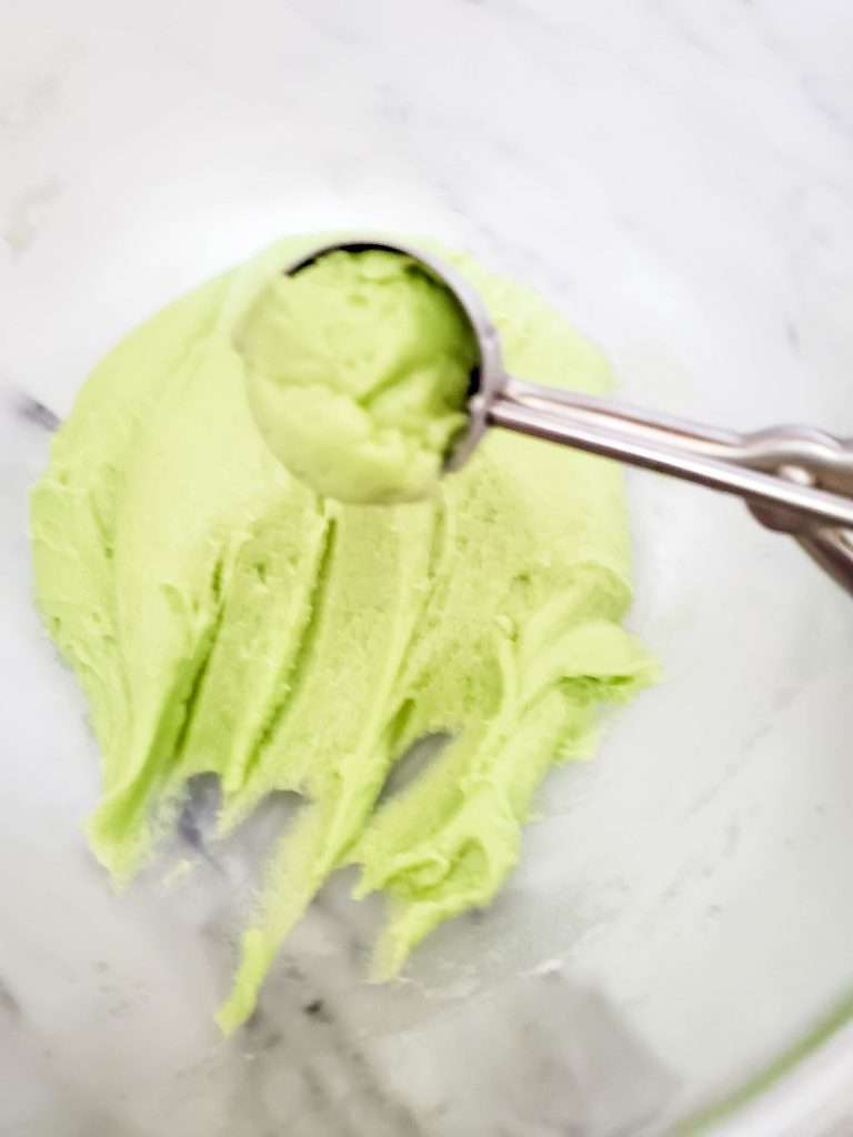 Grinch cookie dough being scooped up with a cookie scoop.