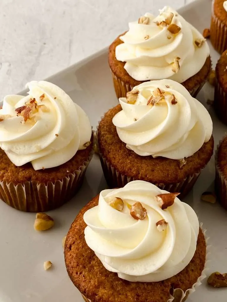 Apple Cider Cupcakes with vanilla frosting and chopped walnuts on a white plate. 