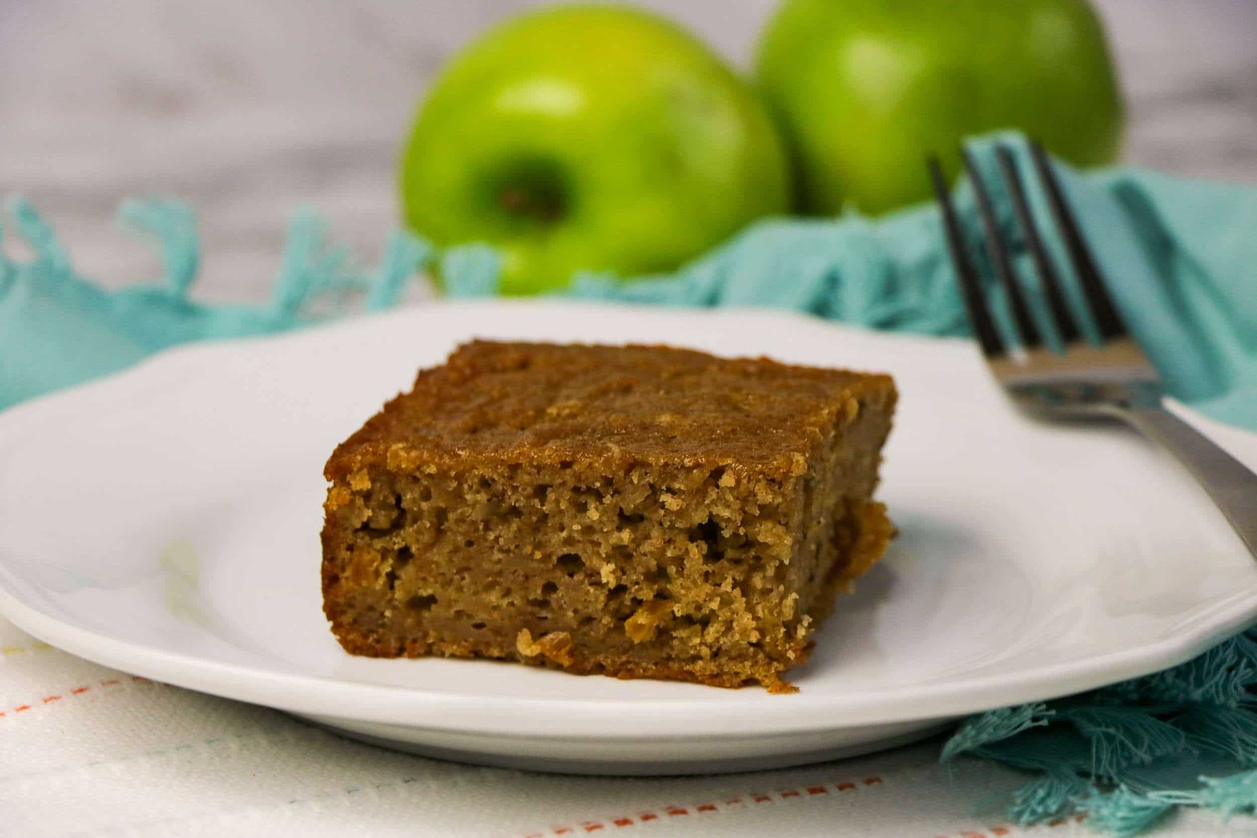 applesauce cake slice on white plate with green apples in the background